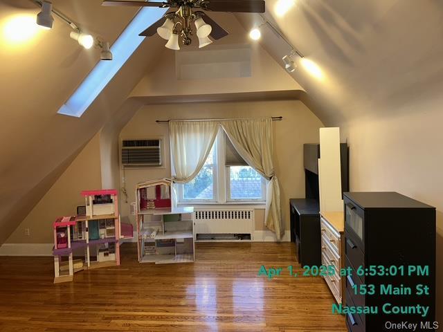 recreation room with lofted ceiling with skylight, wood finished floors, a ceiling fan, radiator, and an AC wall unit
