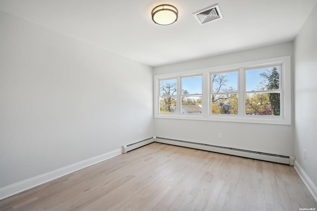 empty room with a healthy amount of sunlight, baseboard heating, and light hardwood / wood-style flooring