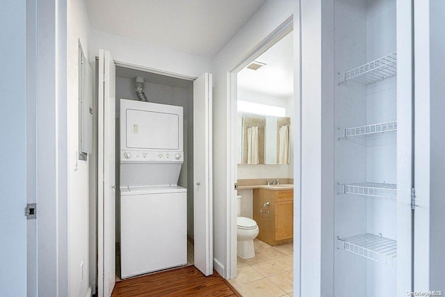 clothes washing area with sink, light tile patterned floors, and stacked washer and dryer