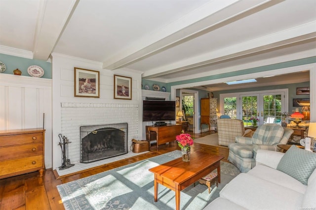 living room with dark hardwood / wood-style floors, beam ceiling, ornamental molding, and a brick fireplace