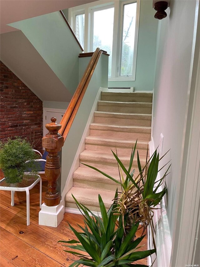 stairs featuring brick wall and hardwood / wood-style flooring