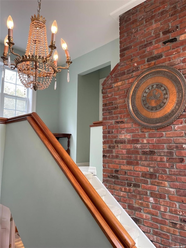 stairway with a notable chandelier and brick wall