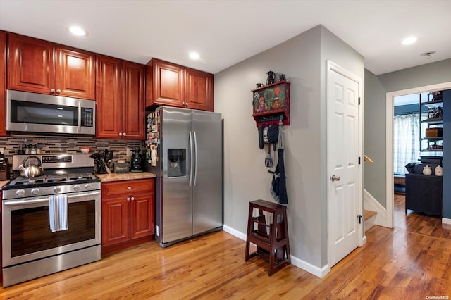 kitchen with tasteful backsplash, light stone counters, light hardwood / wood-style flooring, and appliances with stainless steel finishes