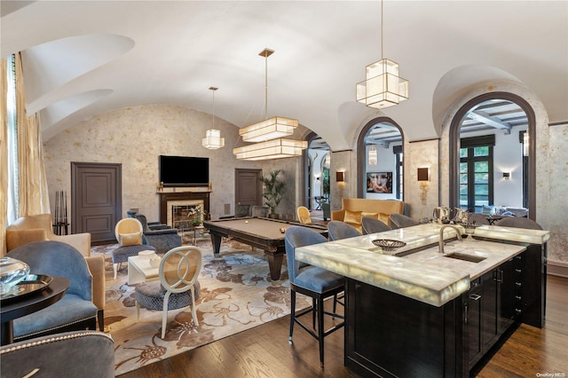 kitchen with dark wood-type flooring, a kitchen island with sink, hanging light fixtures, sink, and pool table