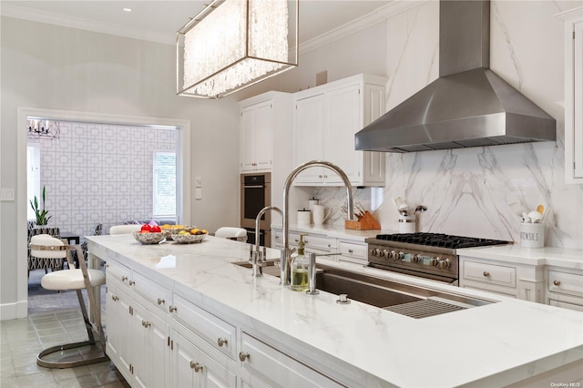 kitchen with wall chimney range hood, an inviting chandelier, decorative light fixtures, white cabinets, and ornamental molding