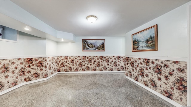 spare room with granite finish floor, baseboards, wainscoting, and wallpapered walls