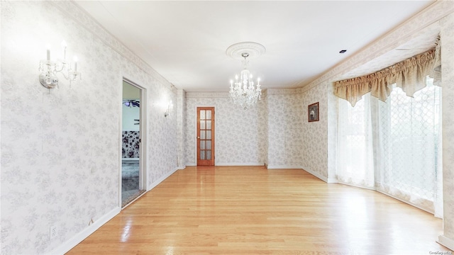 unfurnished room with baseboards, a notable chandelier, wood finished floors, and wallpapered walls