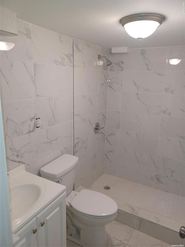 bathroom featuring a tile shower, vanity, toilet, and tile walls