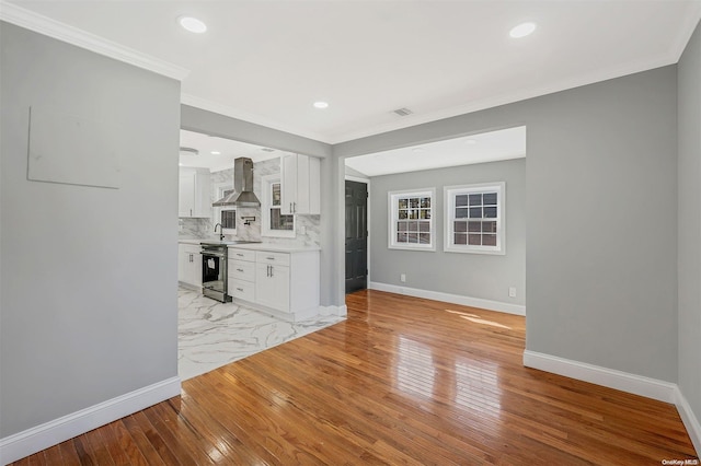 interior space with stainless steel electric range, crown molding, light hardwood / wood-style flooring, wall chimney exhaust hood, and white cabinetry