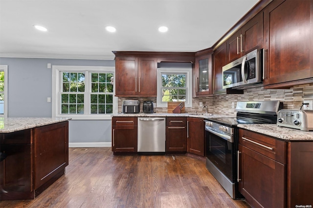 kitchen with appliances with stainless steel finishes, crown molding, dark wood-type flooring, and light stone counters