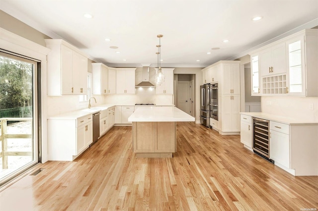 kitchen with wall chimney range hood, wine cooler, light hardwood / wood-style flooring, decorative light fixtures, and a kitchen island