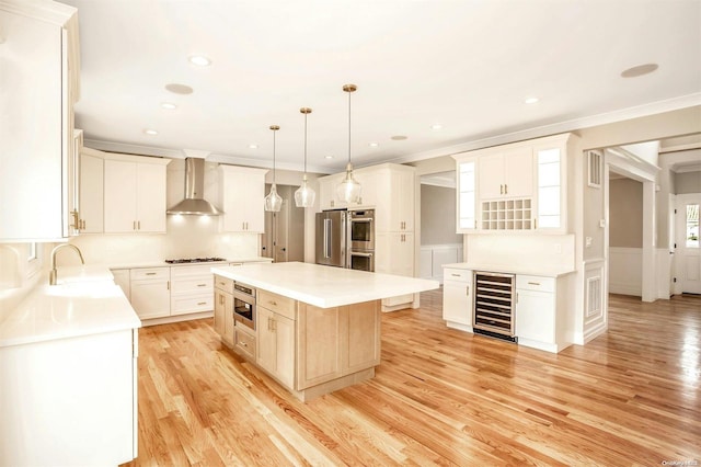 kitchen featuring appliances with stainless steel finishes, wall chimney exhaust hood, beverage cooler, light hardwood / wood-style floors, and a kitchen island