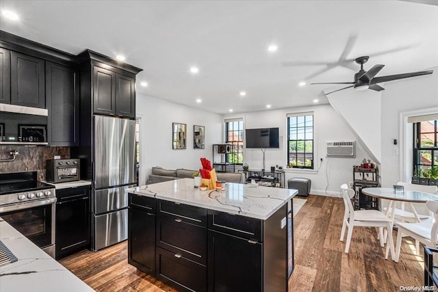 kitchen featuring ceiling fan, a center island, a wall mounted AC, light hardwood / wood-style floors, and appliances with stainless steel finishes