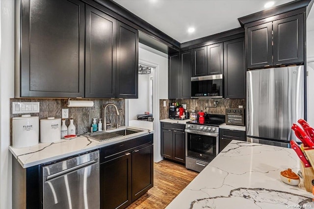 kitchen featuring sink, stainless steel appliances, light stone counters, light hardwood / wood-style flooring, and decorative backsplash