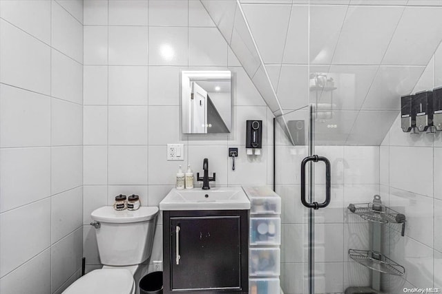 bathroom with vanity, a shower with door, toilet, and tile walls