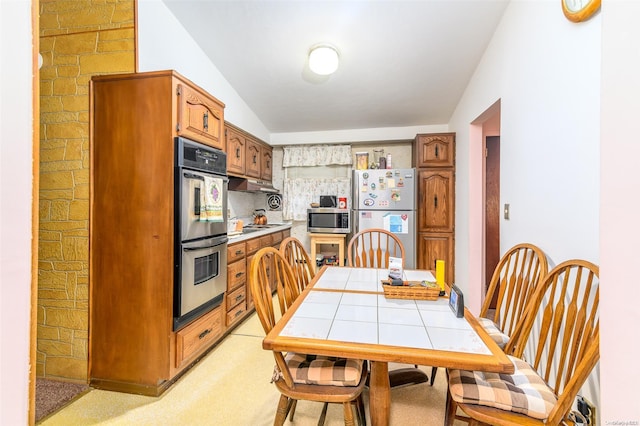 kitchen with appliances with stainless steel finishes, light colored carpet, tile counters, and lofted ceiling