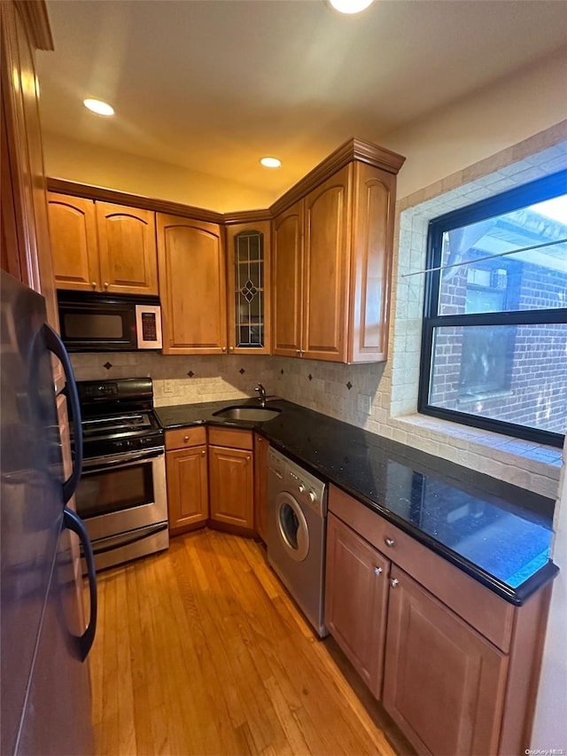 kitchen featuring appliances with stainless steel finishes, sink, dark stone countertops, washer / dryer, and light hardwood / wood-style floors