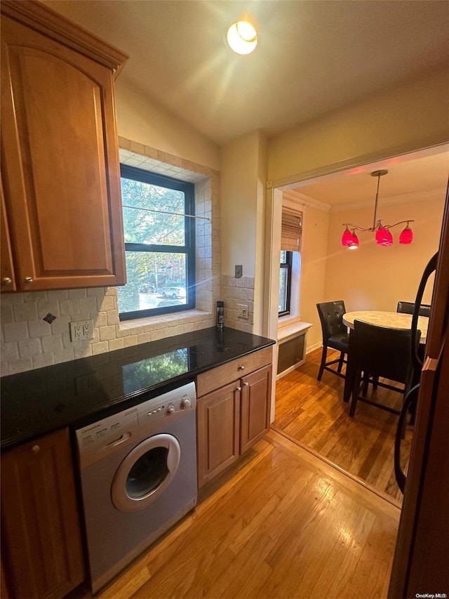 kitchen featuring tasteful backsplash, dark stone counters, decorative light fixtures, washer / dryer, and light wood-type flooring