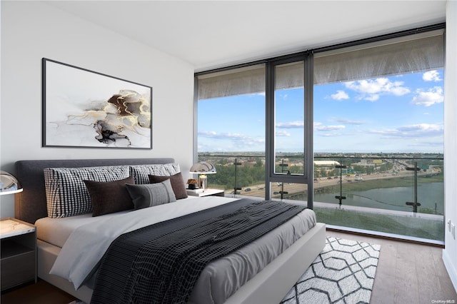 bedroom with a wall of windows, a water view, and hardwood / wood-style flooring