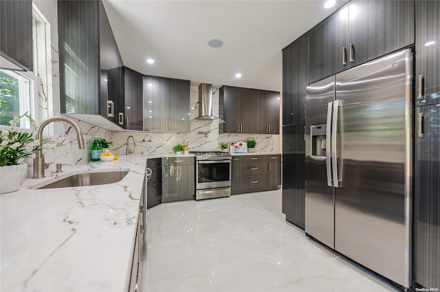 kitchen with sink, wall chimney range hood, tasteful backsplash, light stone counters, and appliances with stainless steel finishes