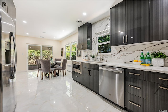 kitchen with decorative backsplash, sink, light stone countertops, and appliances with stainless steel finishes