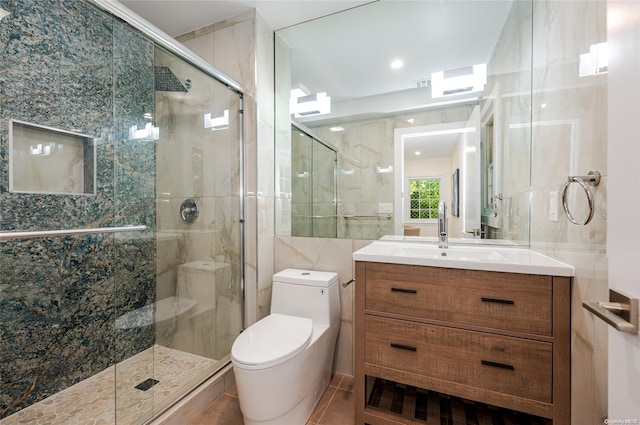 bathroom featuring tile patterned floors, toilet, a shower with door, vanity, and tile walls