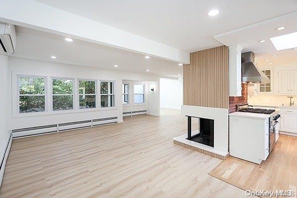 kitchen with white cabinets, stainless steel gas range, backsplash, a baseboard radiator, and wall chimney range hood