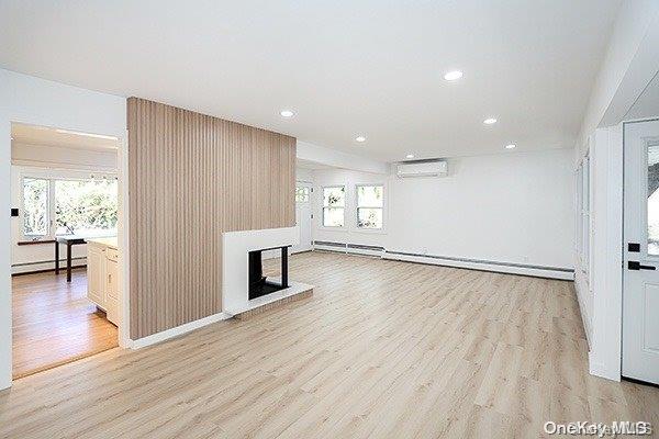 unfurnished living room with a wall unit AC, baseboard heating, and light hardwood / wood-style flooring