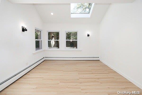 empty room with a baseboard heating unit, lofted ceiling with skylight, and light hardwood / wood-style flooring