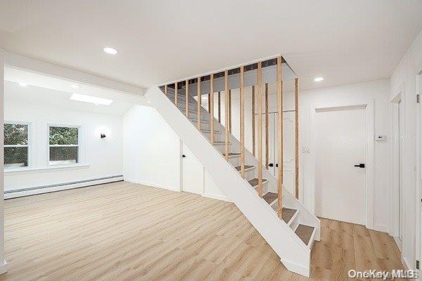 stairs with vaulted ceiling, a baseboard radiator, and hardwood / wood-style flooring