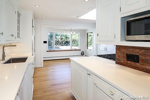 kitchen featuring sink, white cabinetry, light hardwood / wood-style flooring, a baseboard heating unit, and stainless steel microwave