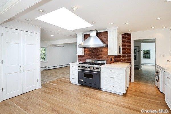 kitchen with wall chimney range hood, baseboard heating, white cabinetry, and high end stove