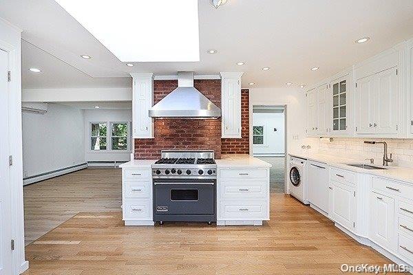 kitchen with stainless steel stove, wall chimney range hood, white cabinets, washer / clothes dryer, and sink