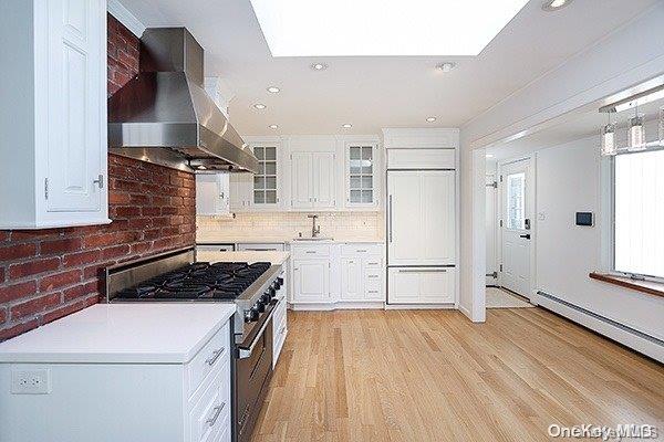 kitchen featuring premium appliances, light wood-type flooring, white cabinetry, ventilation hood, and sink