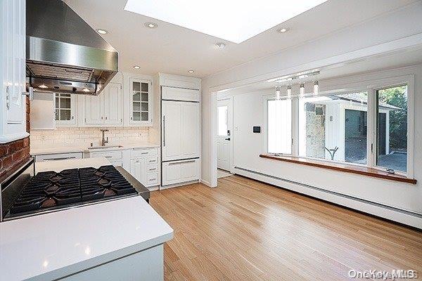 kitchen with exhaust hood, paneled built in refrigerator, a baseboard heating unit, white cabinetry, and sink