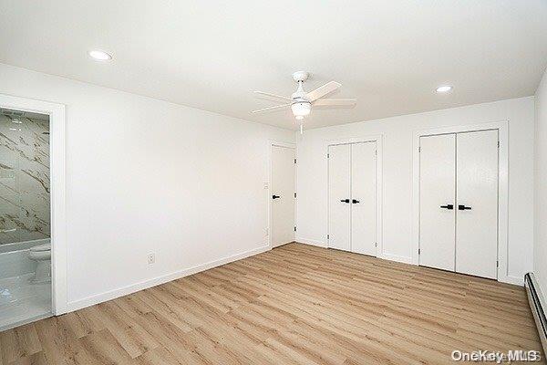 unfurnished bedroom featuring multiple closets, connected bathroom, ceiling fan, light hardwood / wood-style floors, and a baseboard heating unit