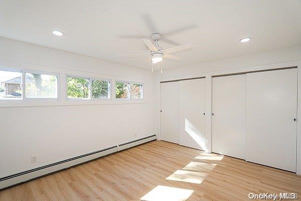 unfurnished bedroom with a baseboard heating unit, light wood-type flooring, ceiling fan, and multiple windows