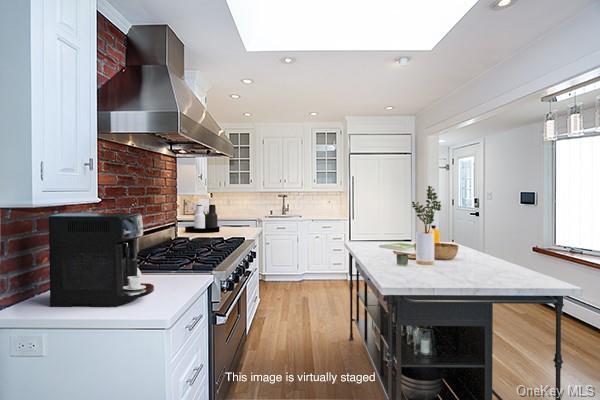 kitchen featuring high end appliances, exhaust hood, a kitchen island, a skylight, and white cabinetry