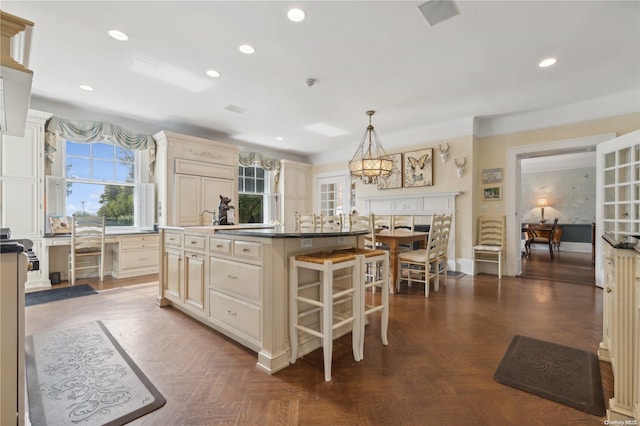 kitchen with a center island with sink, dark parquet floors, pendant lighting, and cream cabinetry