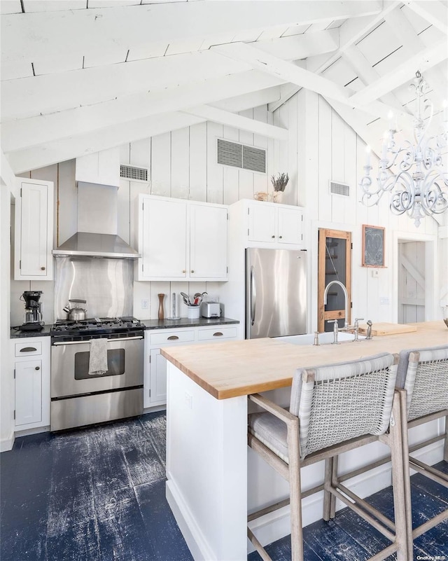 kitchen featuring wall chimney exhaust hood, stainless steel appliances, vaulted ceiling with beams, a kitchen bar, and white cabinets