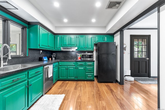 kitchen with sink, tasteful backsplash, green cabinets, appliances with stainless steel finishes, and light wood-type flooring