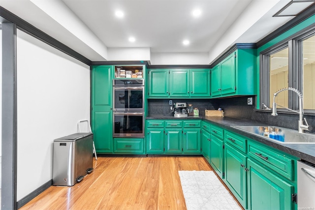 kitchen with sink, stainless steel appliances, green cabinets, backsplash, and light hardwood / wood-style floors