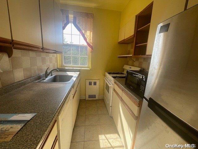 kitchen with stainless steel fridge, radiator, sink, light tile patterned floors, and white stove