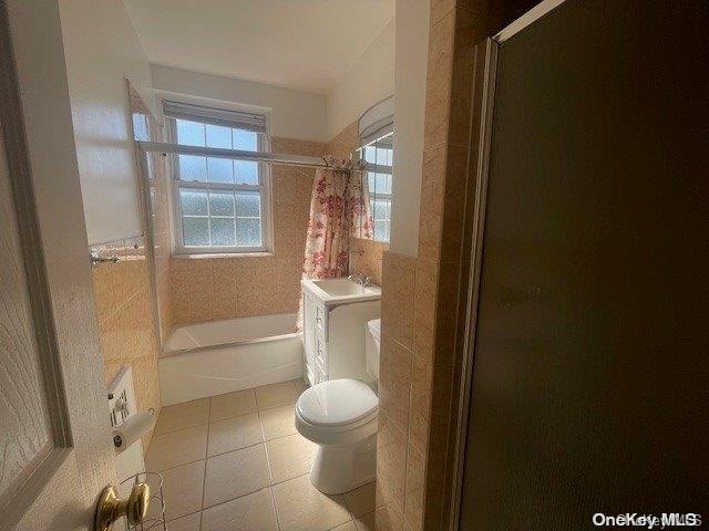 bathroom with tile patterned flooring, shower / bath combination, toilet, and tile walls