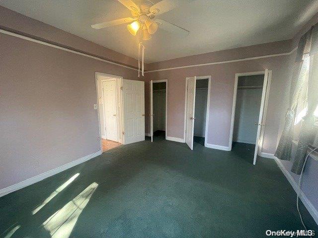 unfurnished bedroom featuring dark colored carpet, two closets, and ceiling fan