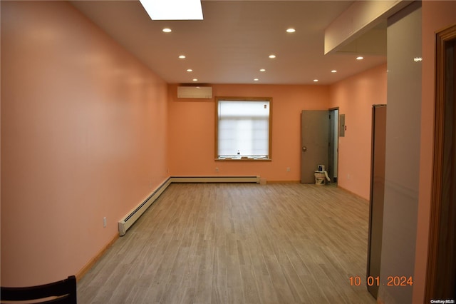 unfurnished room featuring light hardwood / wood-style flooring, baseboard heating, and an AC wall unit