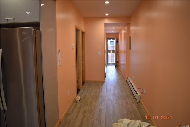 corridor with light wood-type flooring and a baseboard heating unit