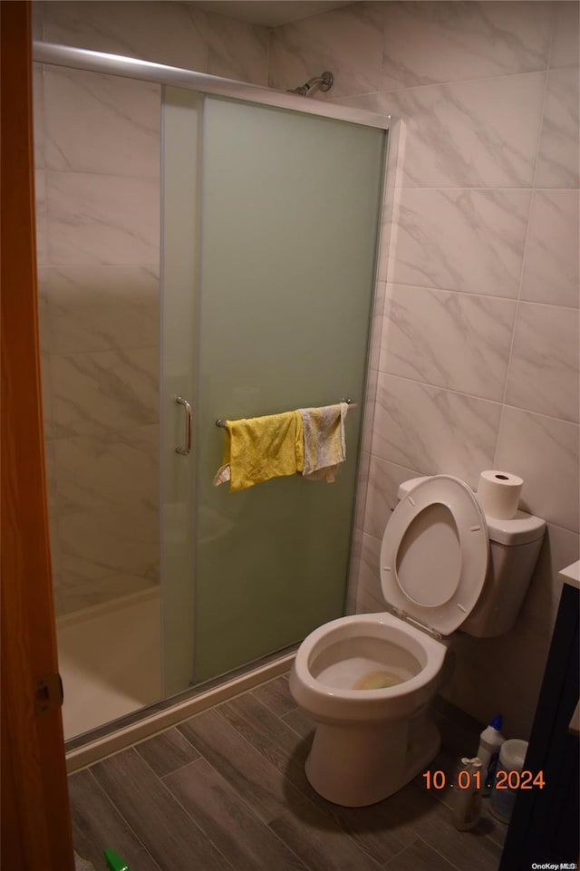 bathroom with toilet, a shower with shower door, and tile walls