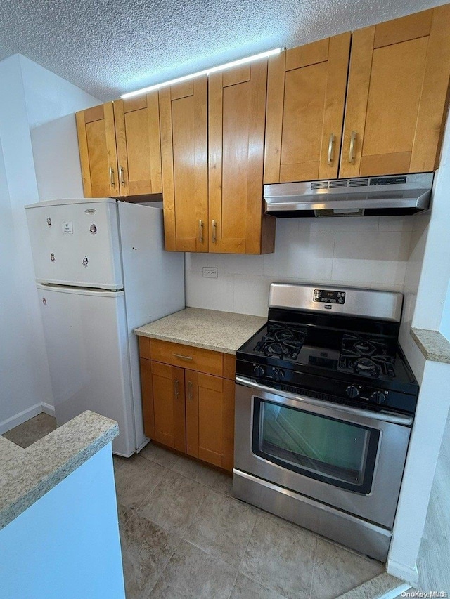 kitchen featuring gas range, decorative backsplash, a textured ceiling, and white refrigerator