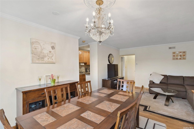 dining space with a chandelier, ornamental molding, and light wood-type flooring